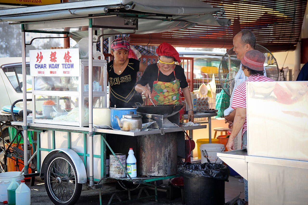A Penang char koay teow hawker cooking beside customers at a street food cart